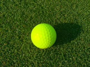 Isolated bright green golf ball site on golf course grass waiting for player to putt into hole for par score. Morning sunrise shadow cast on fairway.