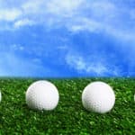 Golf balls on green grass against blue sky background