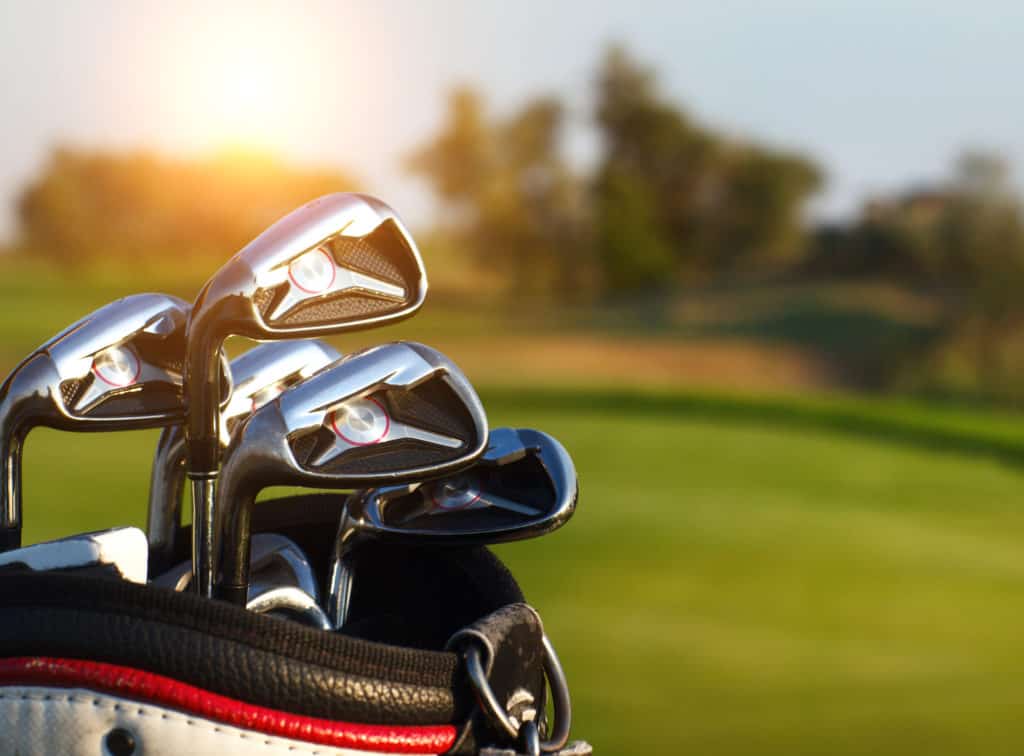 Golf clubs drivers over green field background. Summer sunset