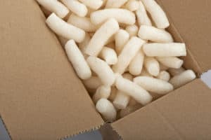 Cardboard box with yellow packing styrofoam peanuts, isolated on white background.