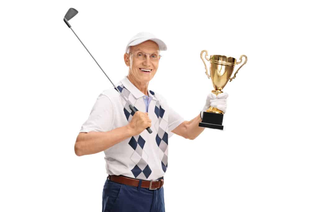 Joyful senior golfer holding a gold trophy and looking at the camera isolated on white background