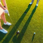 High-angle cropped view of a professional woman player holding the putter golf club, ready to hit the ball into the hole at the end of a difficult game with her partner or instructor