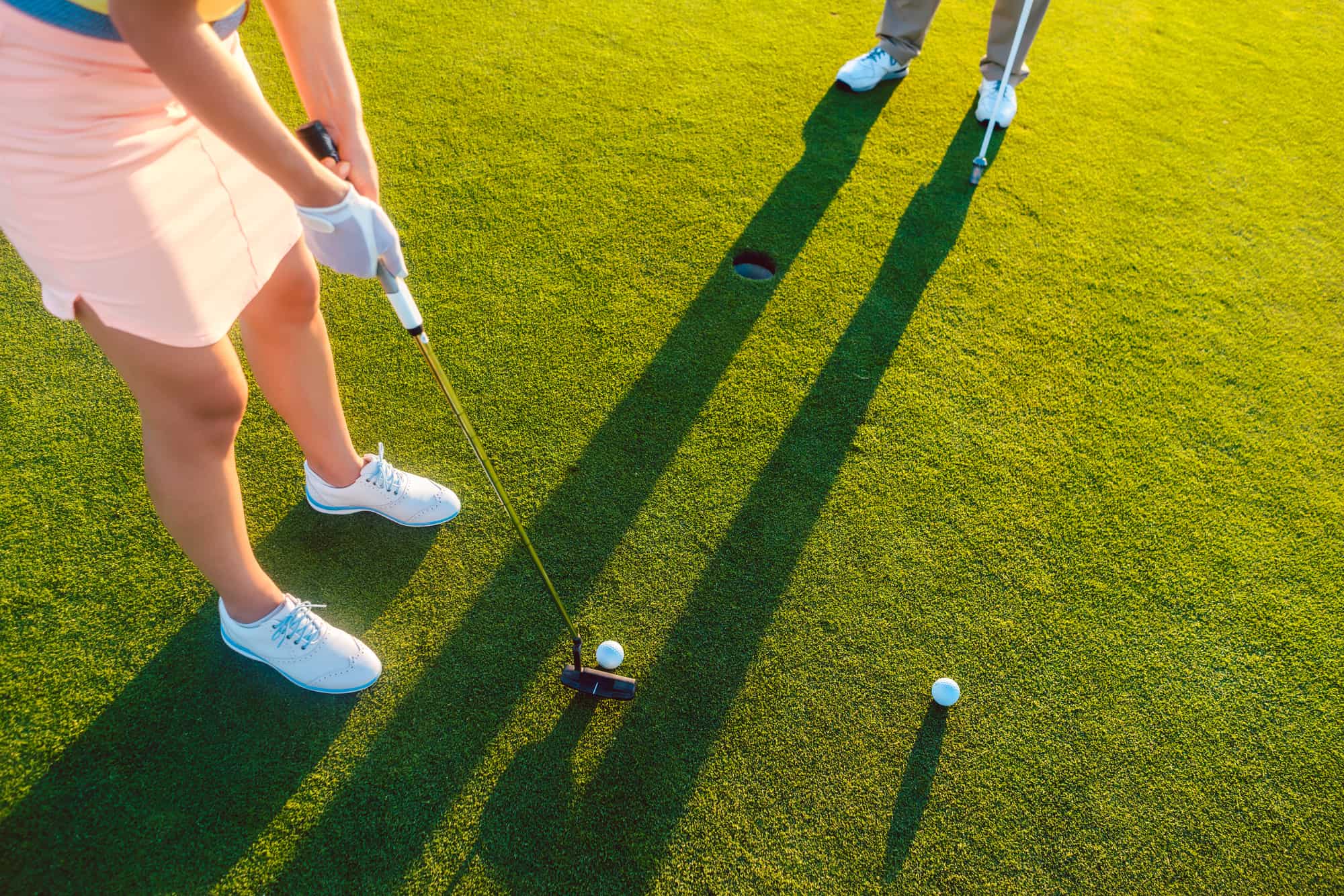 High-angle cropped view of a professional woman player holding the putter golf club, ready to hit the ball into the hole at the end of a difficult game with her partner or instructor