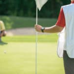 Golfer putting from long distance, reading green, caddy holding golf flag
