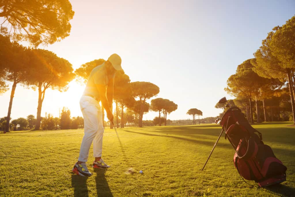 golf player hitting shot with club on course at beautiful morning with sun flare in background