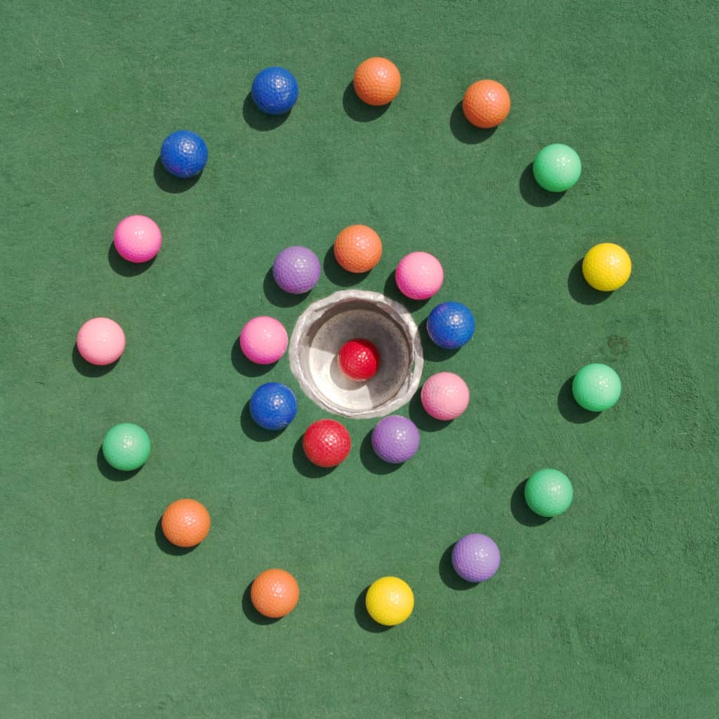 Two concentric circles of golf balls surrounding a hole with a red golf ball that's made a hole-in-one.