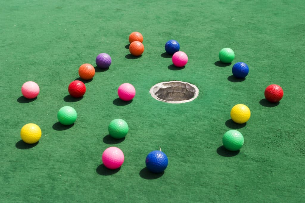 A number of brightly colored golf balls scattered around the hole on a practice putting green.