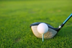 Golf tee ball club driver in green grass course closeup