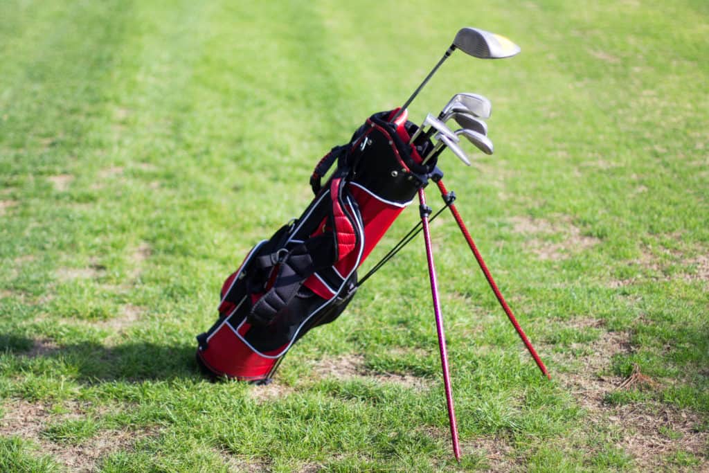 A golf bag with clubs standing on the grass on a sunny day