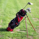 A golf bag with clubs standing on the grass on a sunny day