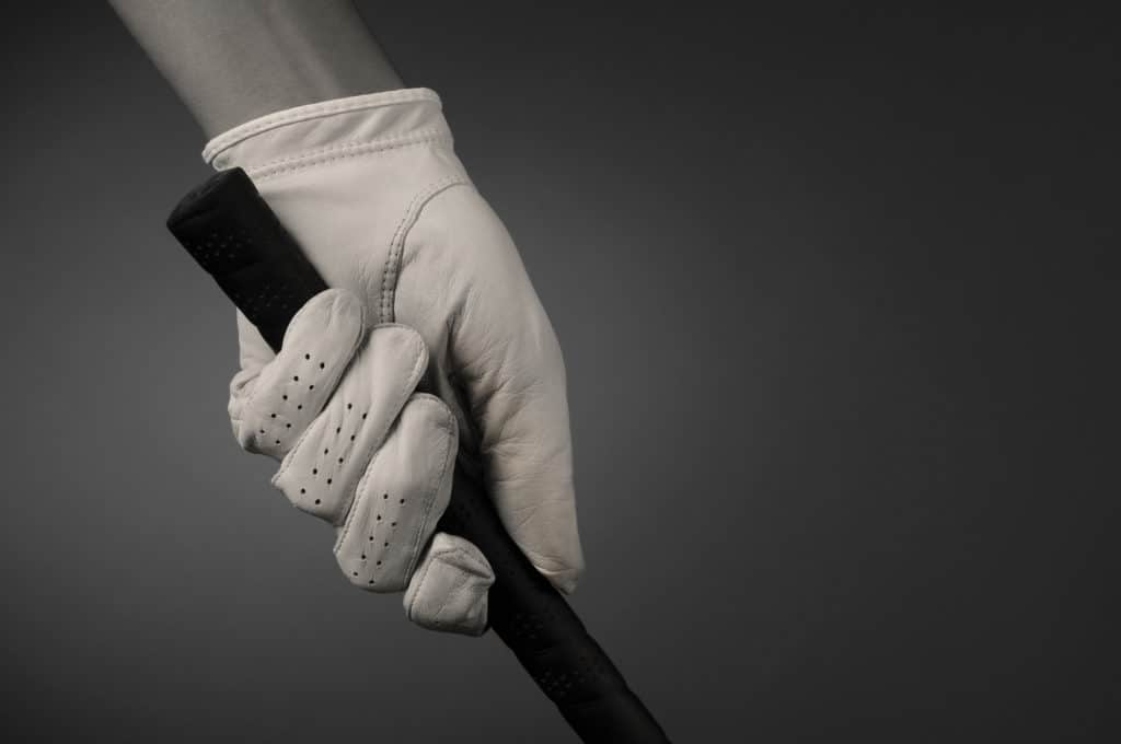 Closeup of a golfers hand on the handle of a golf club. Horizontal format on a light ot dark background. Slight sepia toning for an old fashioned look.