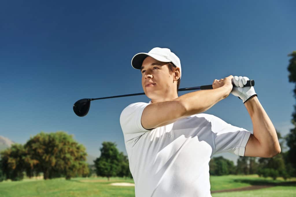 Golfer hitting driver club on course for tee shot