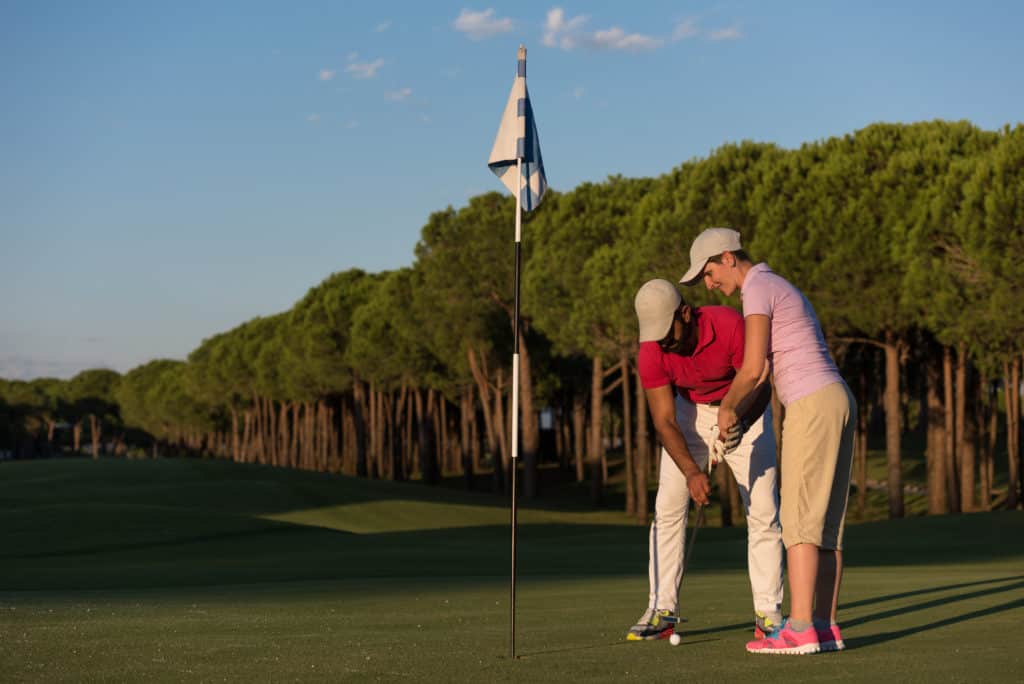 male golf instructor teaching female golf player, personal trainer giving lesson on golf course