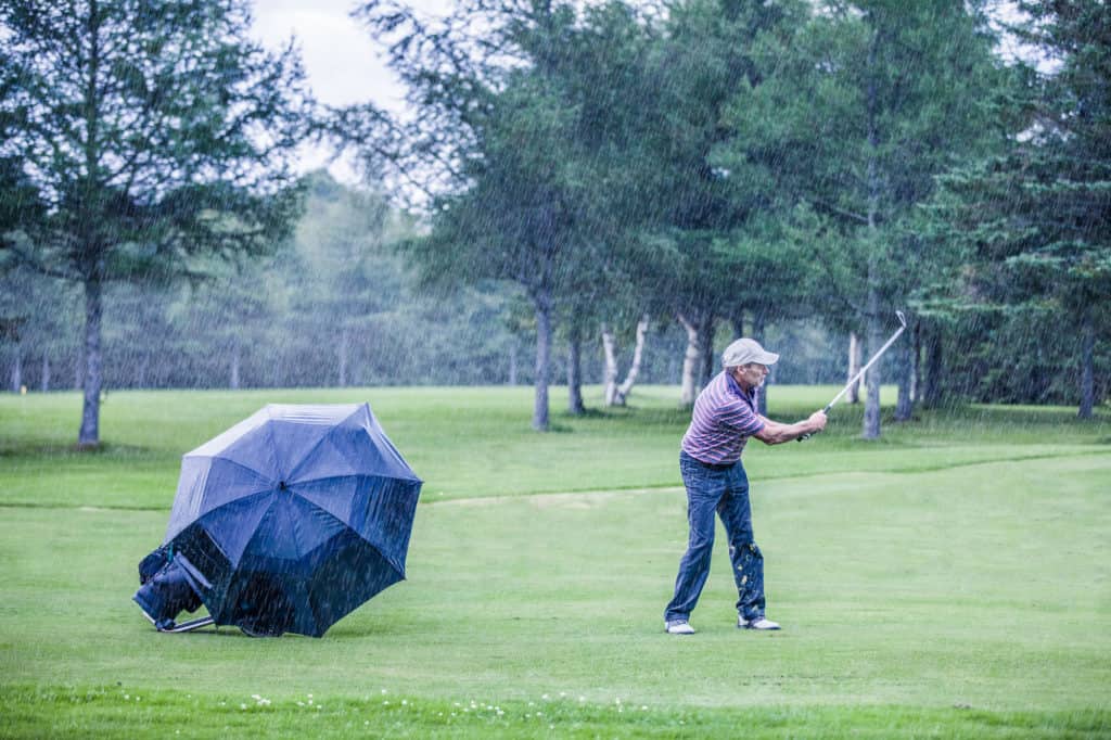 Golfer on a Rainy Day Swigning in the Fairway (motivation concept)