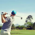 Golfer hitting golf shot with club on course while on summer vacation