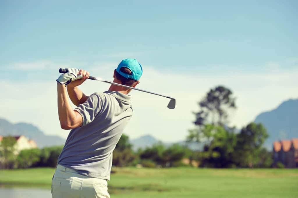 Golfer hitting golf shot with club on course while on summer vacation