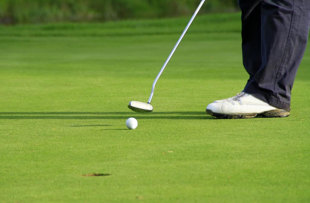 player putting golf ball on putting green