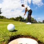 Golfer drove the ball into the hole on putting green; summer sunny day, selective focus on ball