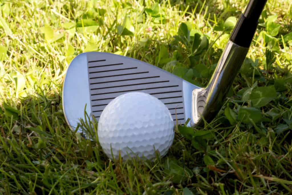 Iron golf club and golf ball in the rough golf course grass