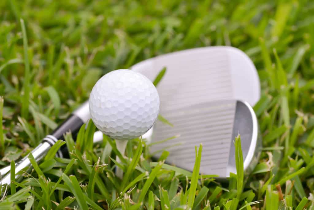 Golf irons and ball on a tee laying on the fairway grass