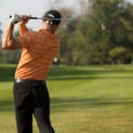 Young man swinging golf club, rear view