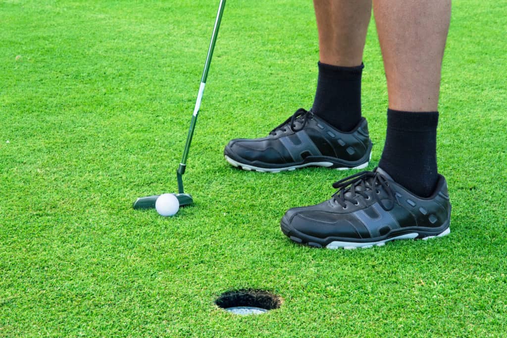 Feet of a male golfer putting at green, closeup