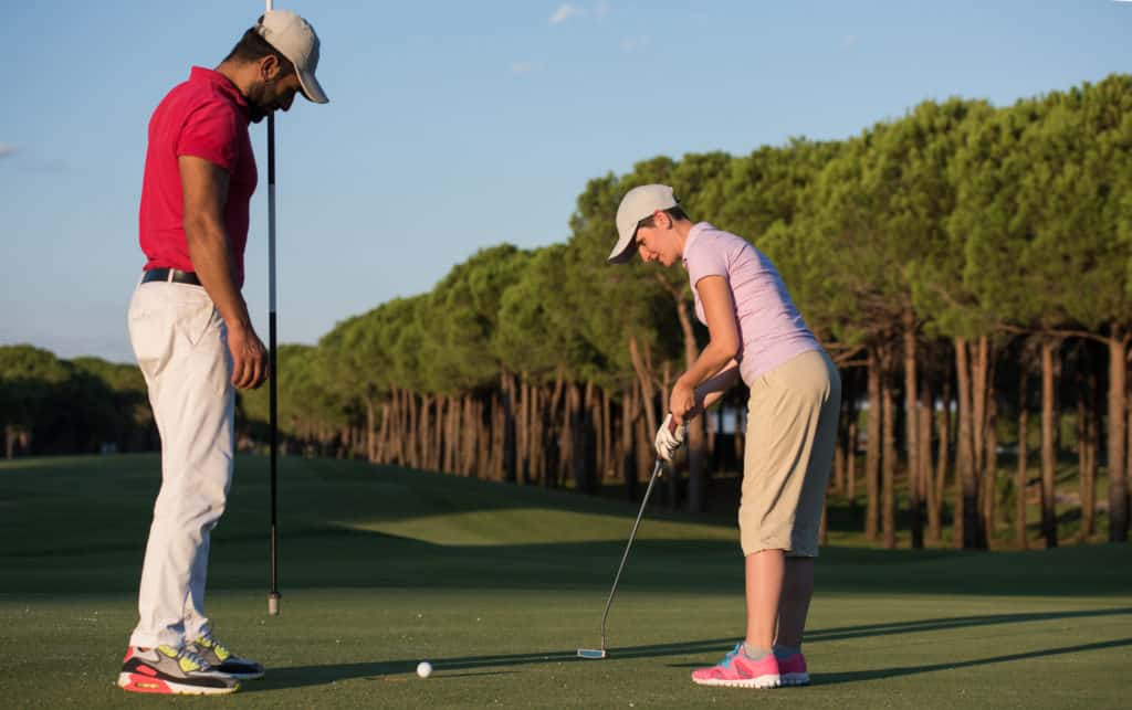 male golf instructor teaching female golf player, personal trainer giving lesson on golf course