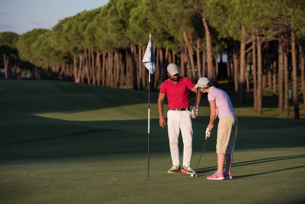 male golf instructor teaching female golf player, personal trainer giving lesson on golf course