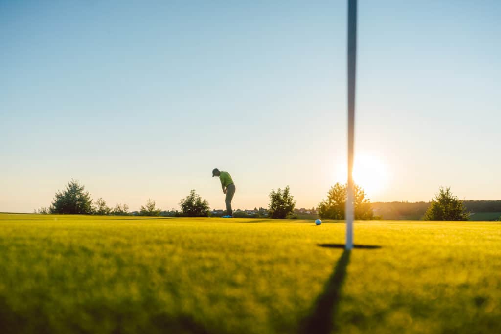 Full length view of the silhouette of a male player, hitting a long shot on the putting green of a professional golf course of a modern country club