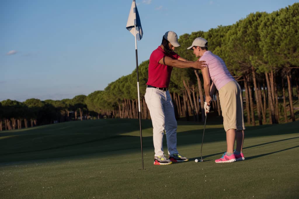 male golf instructor teaching female golf player, personal trainer giving lesson on golf course