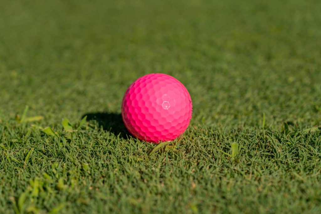 Pink colored golf ball on the edge of the putting green as concept for women golfers