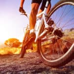 low angle view of cyclist riding mountain bike on rocky trail at sunrise