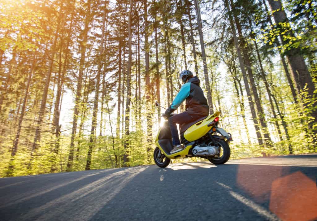 Man riding scooter on forest road. Spring season.