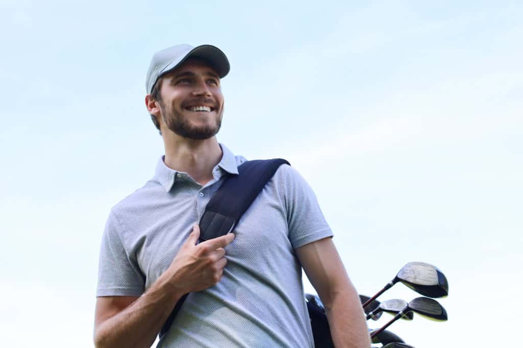 Golf player walking and carrying bag on course during summer game golfing