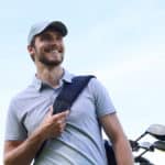 Golf player walking and carrying bag on course during summer game golfing