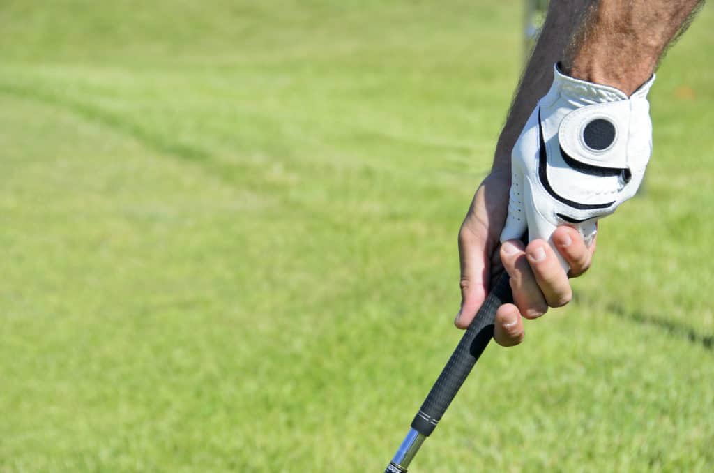 Hands holding a golf stick on of them with the glove in a blurred grass backgound