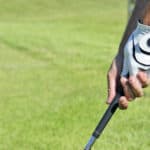 Hands holding a golf stick on of them with the glove in a blurred grass backgound
