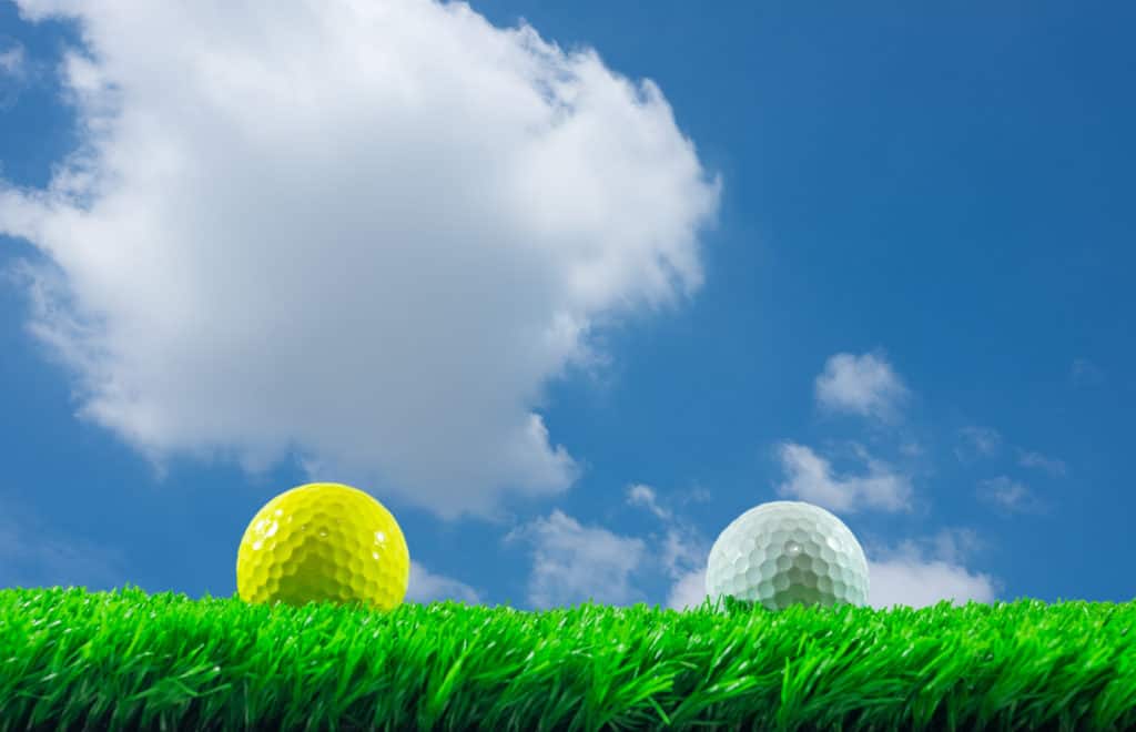 White and yellow golf balls on green artificial grass in blue sky background