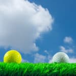 White and yellow golf balls on green artificial grass in blue sky background