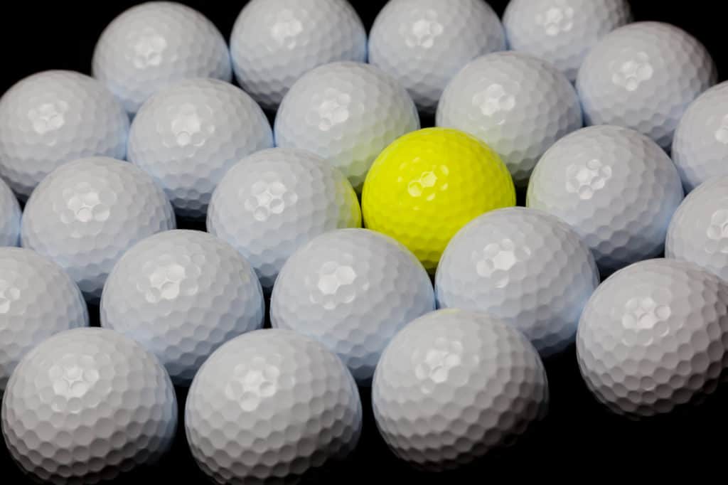 Single yellow golf ball mixed with many white balls. Alternative concept.