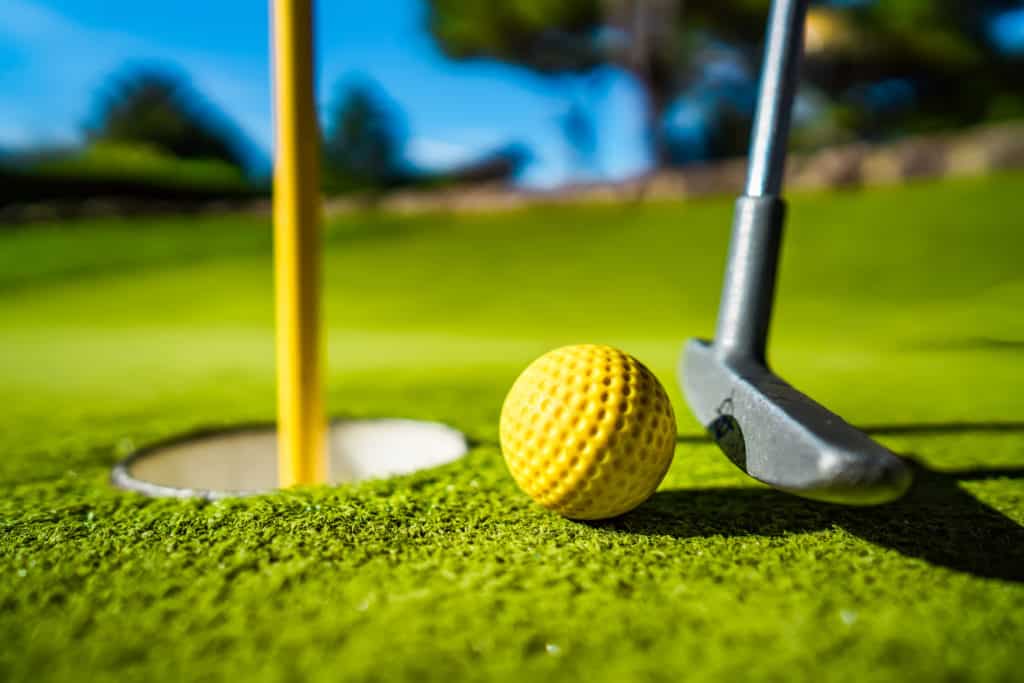 Mini Golf yellow ball with a bat near the hole at sunset