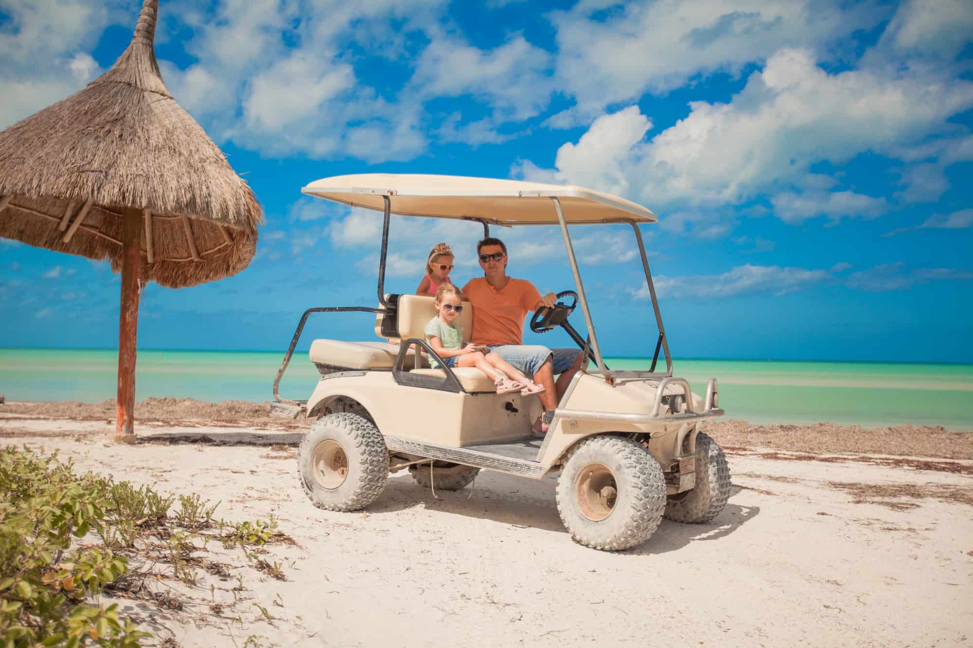 Dad and his two daughters driving golf cart on a tropical beach