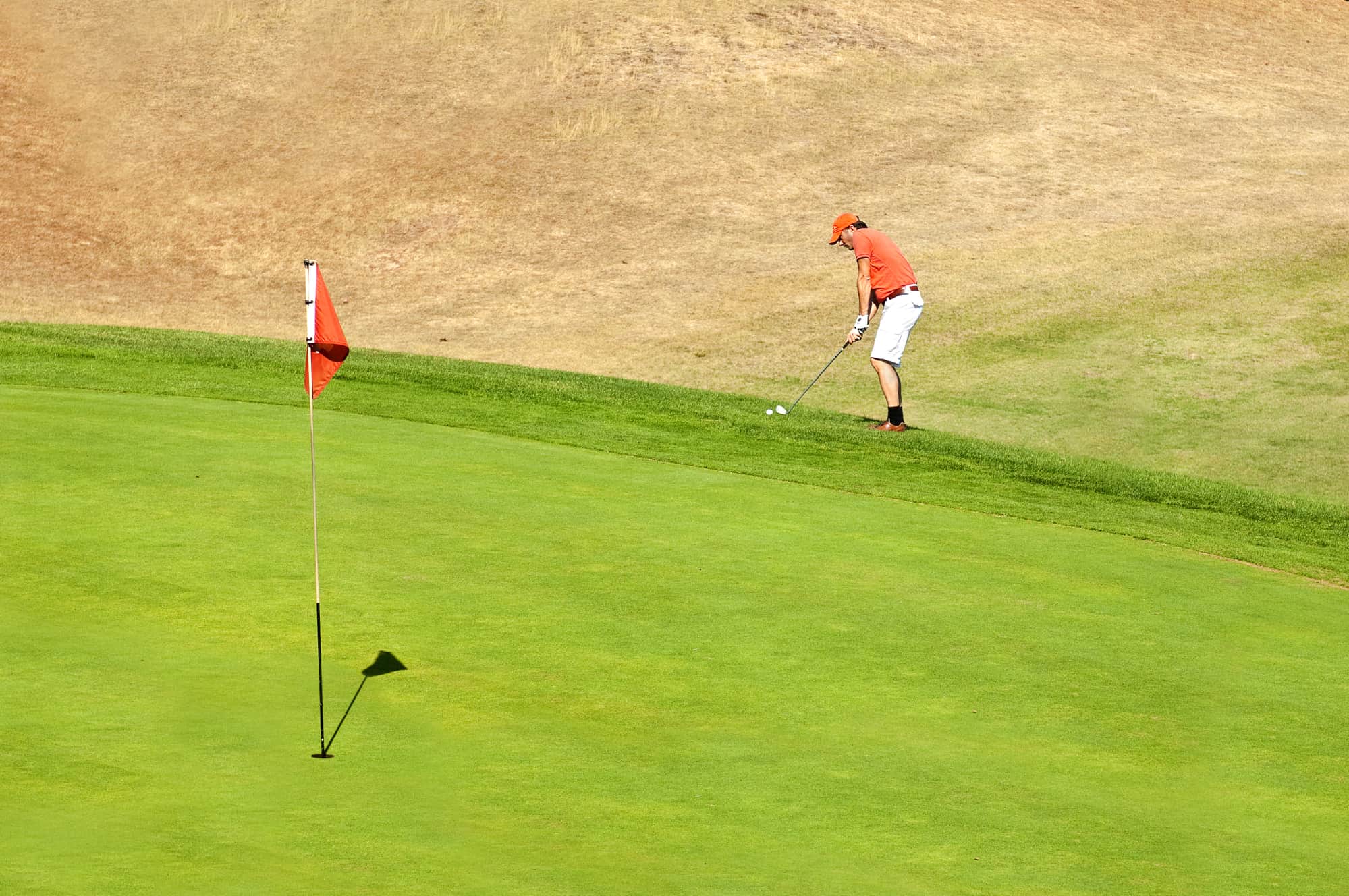 Golf player using a wedge to put his ball on the green near the hole