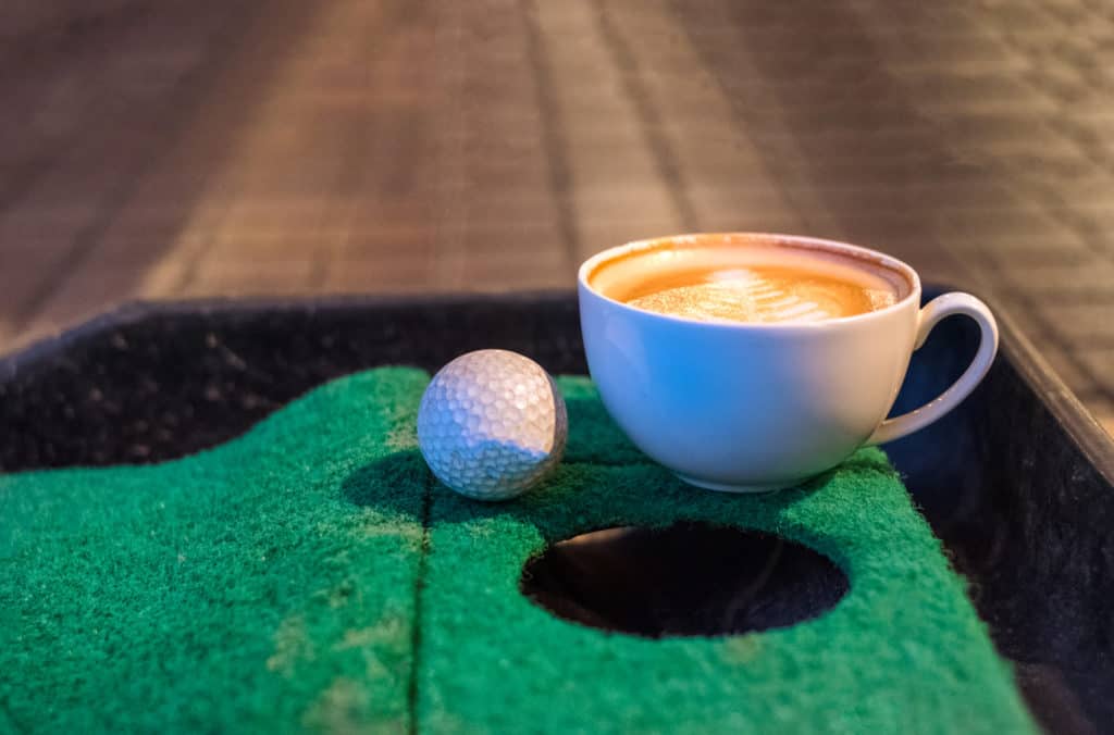 Hot latte coffee cup with golf ball on putting green mat