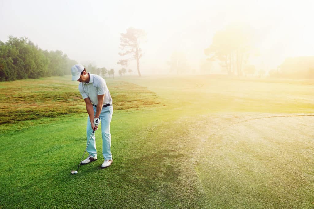 Golfer chipping onto the green at sunrise on the golf course in misty conditions