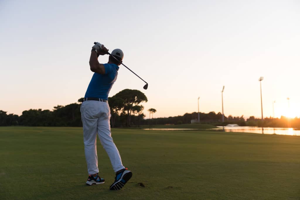 golfer hitting long shot with driver on course at beautiful sunset