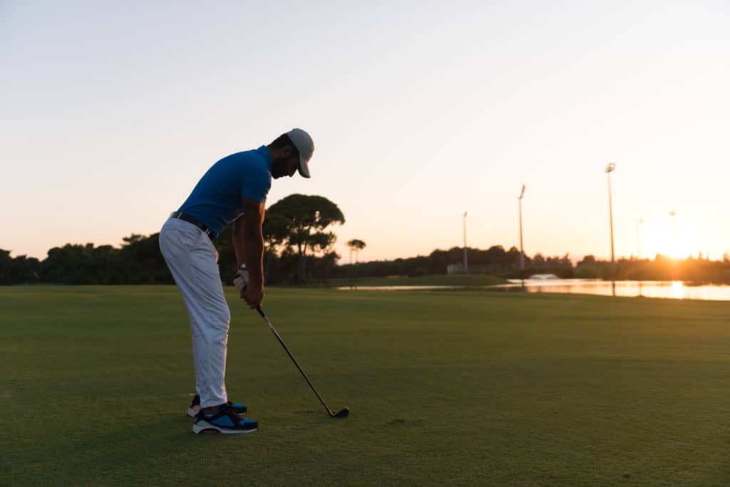 golfer hitting long shot with driver on course at beautiful sunset