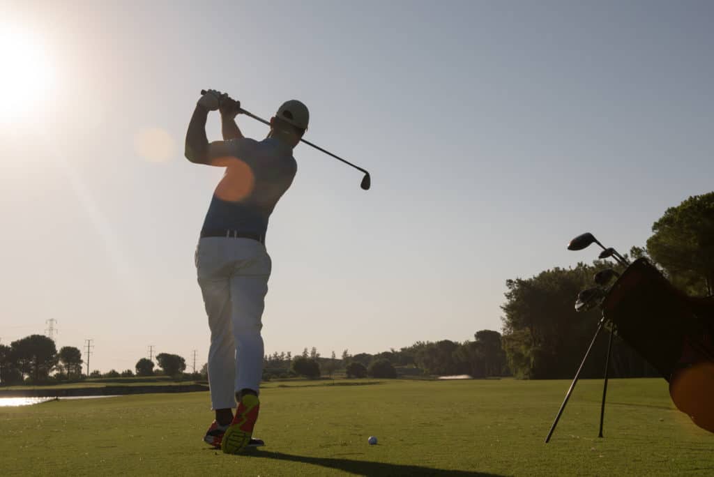 golf player hitting shot with club on course at beautiful morning with sun flare in background