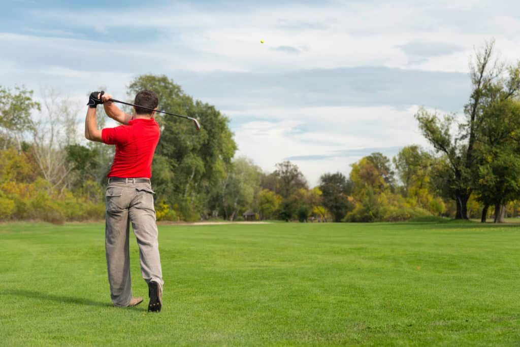 Golfer playing from on a long hole, golf ball visible in the air