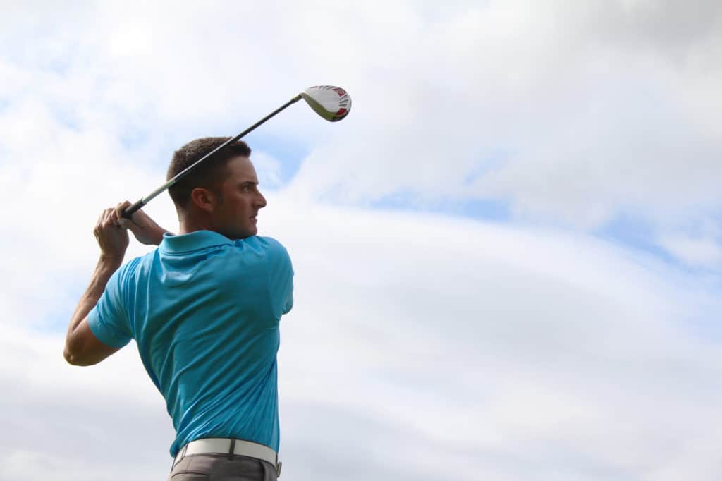 Young golfer driving with a wood against cloudy skies